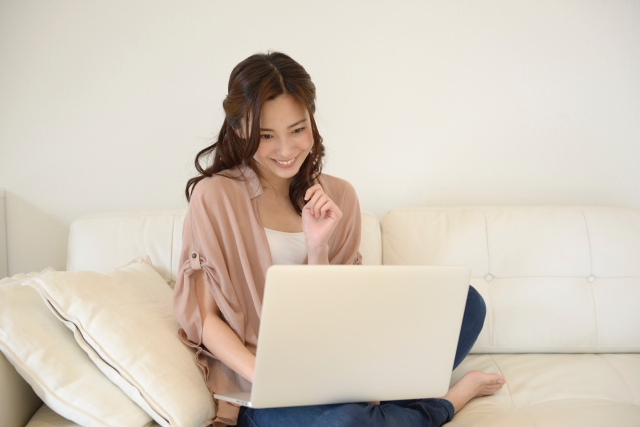 若い女性がソファに座ってパソコンを触っている画像